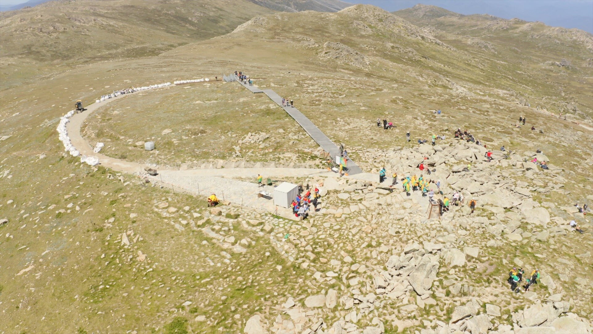 a drone shot of the top of a mountain, with a few people walking around the summit