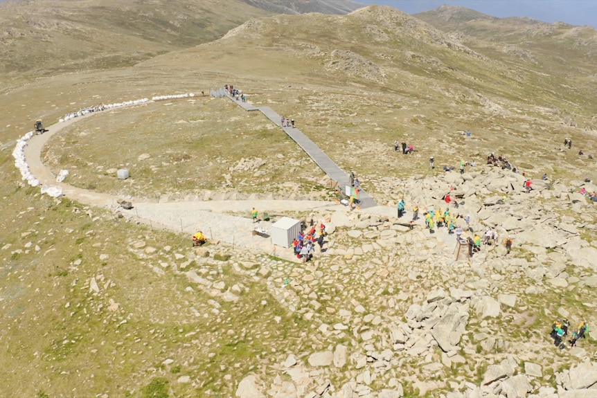 a drone shot of the top of a mountain, with a few people walking around the summit
