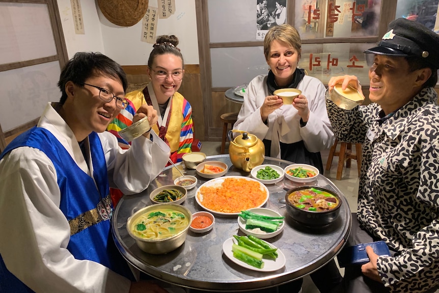 Leesa, Cleo, Heetae, Solri and Pine standing outside a Korean restaurant in traditional clothing.