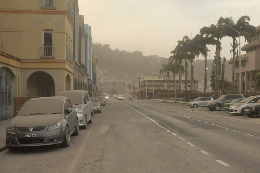 A city street with cars covered in ash and air cloudy.