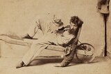 An 1800s sepia-coloured photo of a drunken man in a wheelbarrow