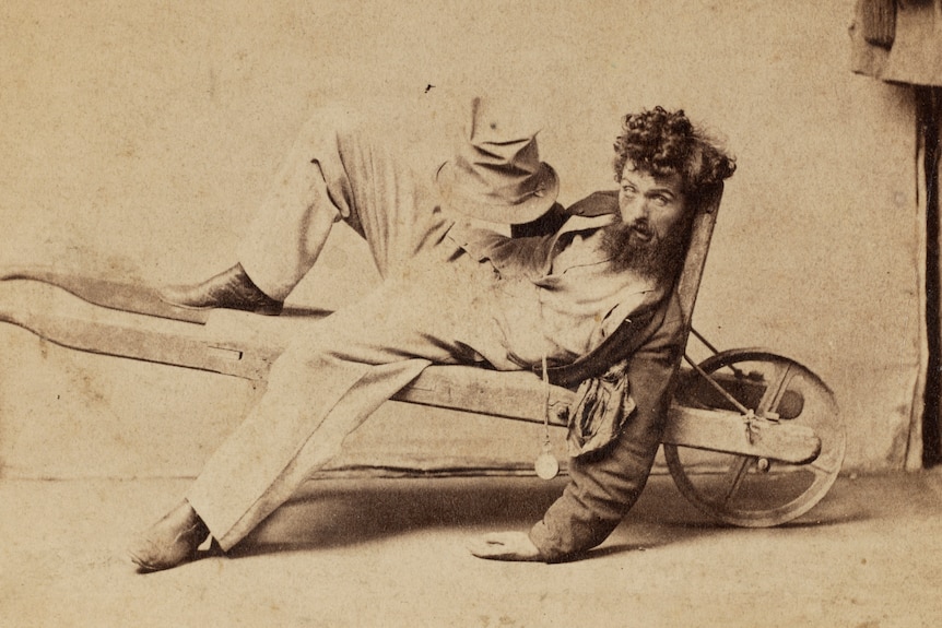 An 1800s sepia-coloured photo of a drunken man in a wheelbarrow