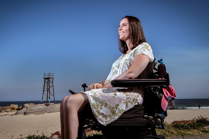 Jess Collins in her wheelchair on the beach, with blue skies in the background.