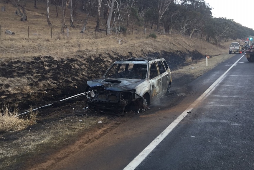 A burnt car sitting beside the Monaro Highway, surrounded by burnt bushland.