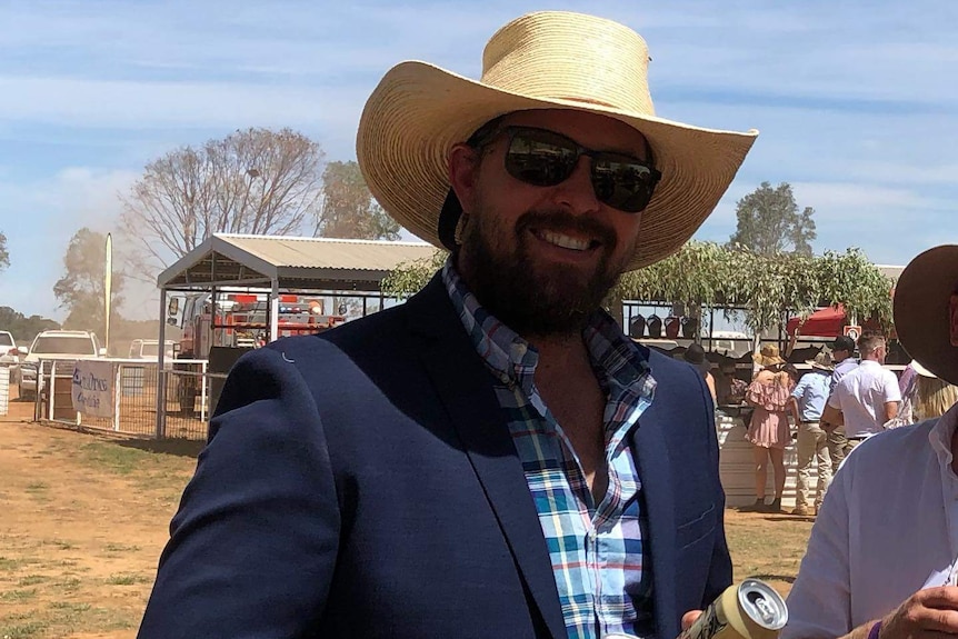 A young man wearing a straw hat and suit, smiling while holding two cans of beer