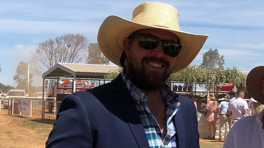 A young man wearing a straw hat and suit, smiling while holding two cans of beer