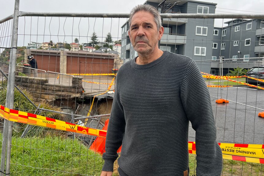 An older man looks solemnly outside a sinkhole, which is separated by a working fence