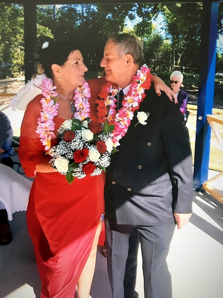 A woman in her 60s wears a red dress and a lay looks into the eyes of a man in a suit.