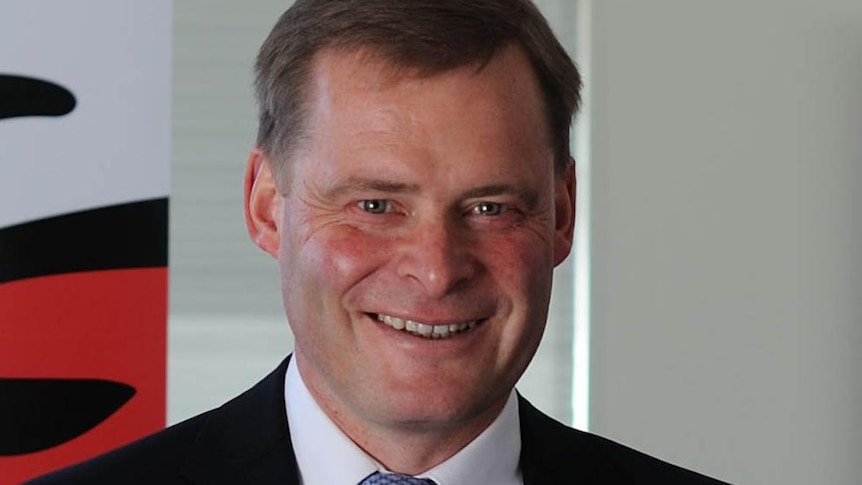 Peter Rathjen smiles and stands in front of a banner with the UTAS logo on it