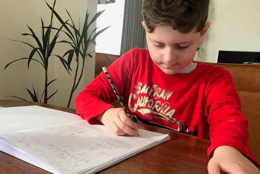 A seven-year-old boy in a red t-shirt working at a desk.