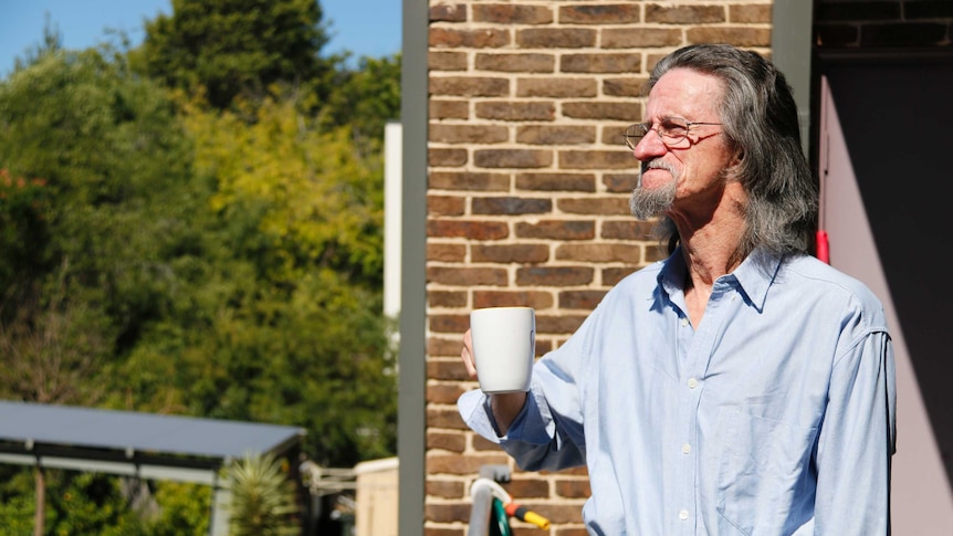 Public housing tenant Peter Marris drinks coffee on his balcony and looks into the distance.