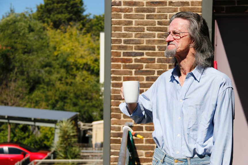 Public housing tenant Peter Marris drinks coffee on his balcony and looks into the distance.