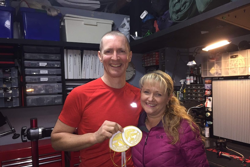 Troy and Nyree Szczurkowski smile for a photo, Troy holds up two patches