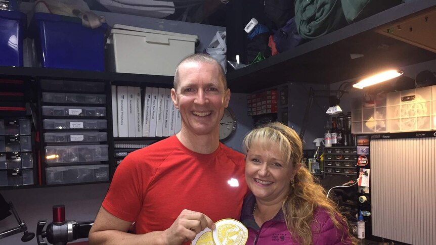 Troy and Nyree Szczurkowski smile for a photo, Troy holds up two patches