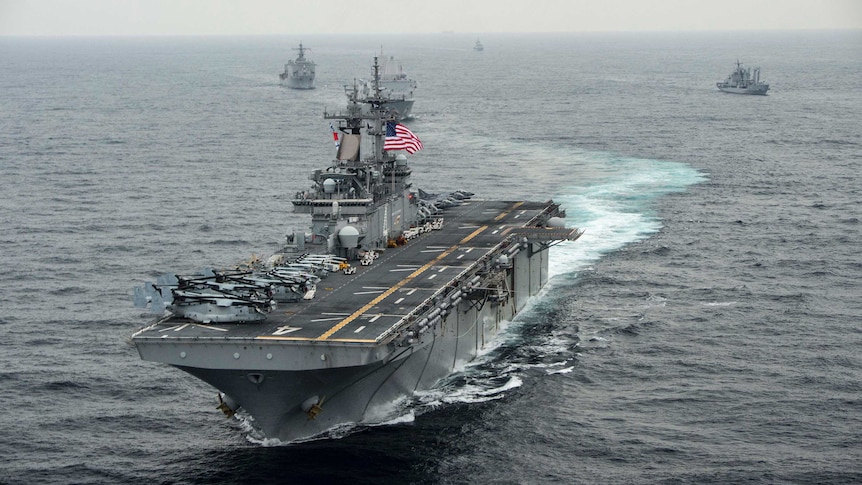 A navy assault ship at sea that has two American flags