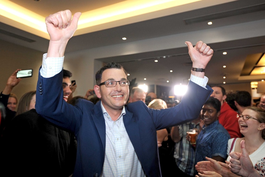 A man stands in a middle of a crowd with his arms raised and his thumbs up.