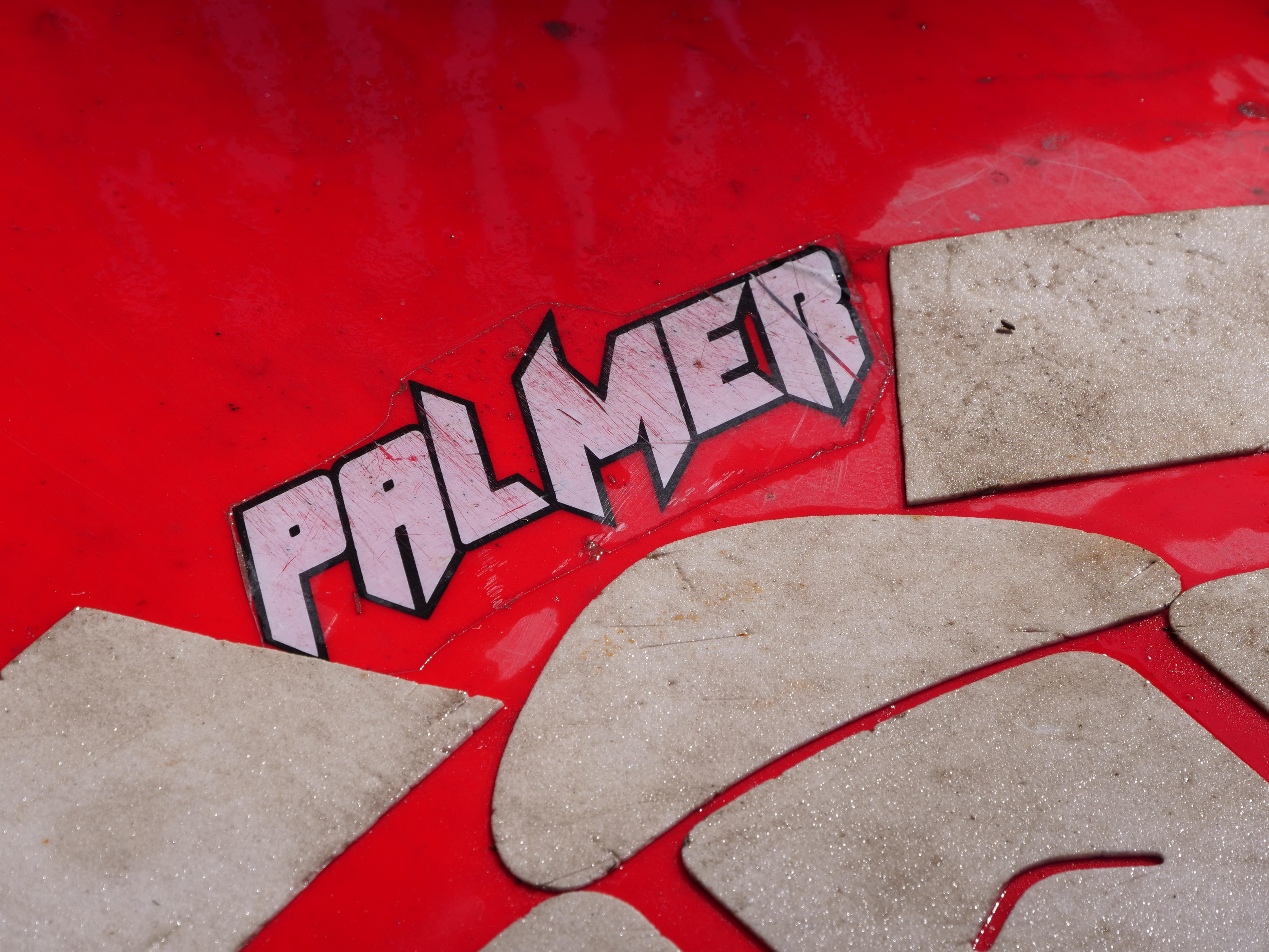 Primer plano de una tabla de surf roja usada con texto blanco y un contorno negro que dice 