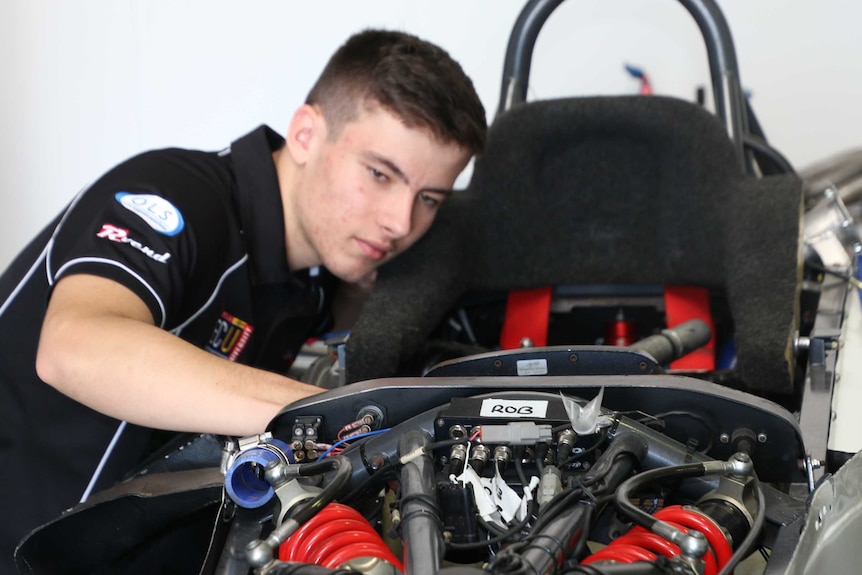 Calan Williams looks over the exposed engine of a red and black racing car