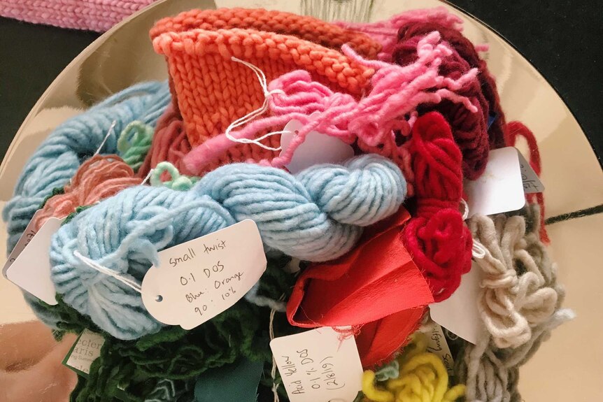 Different coloured samples of wool in a bowl, some with tags on them.