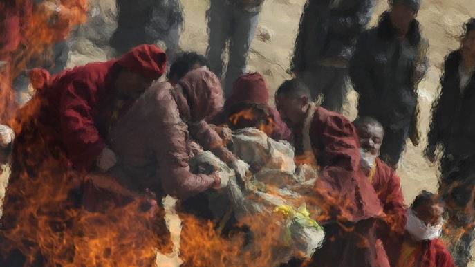 Tibetan Buddhist monks throw the body of an earthquake victim on the fire of a mass cremation