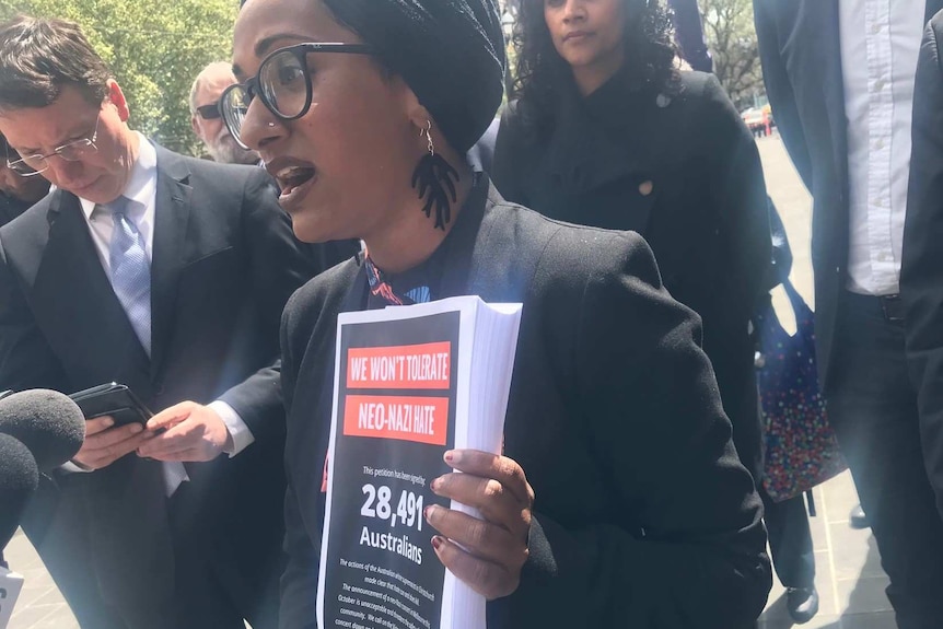 A woman holds a petition and talks to media.