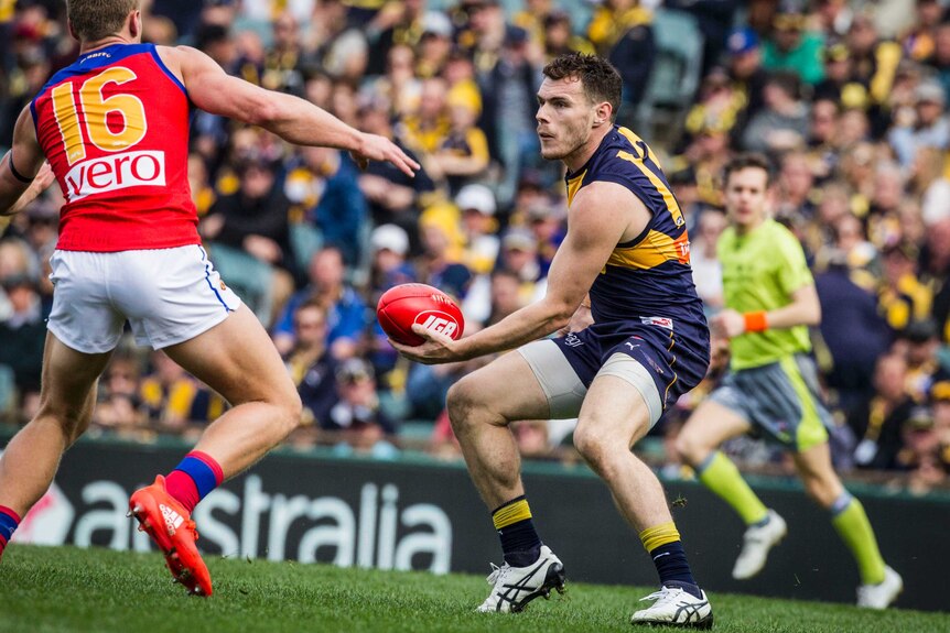 Luke Shuey looks to handball under pressure from a Lions opponent.