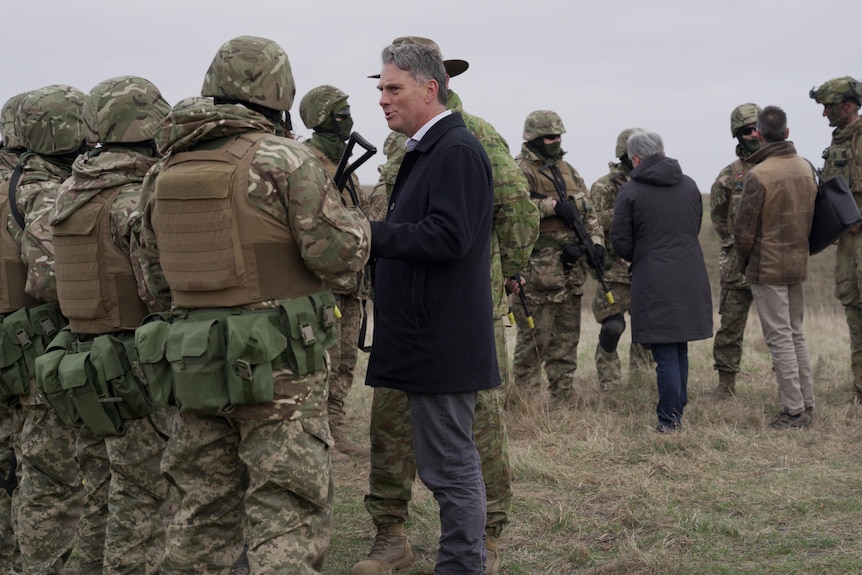 Marles, in a suit, stands with a group of uniformed soldiers, talking.