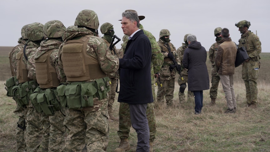 Marles, in a suit, stands with a group of uniformed soldiers, talking.