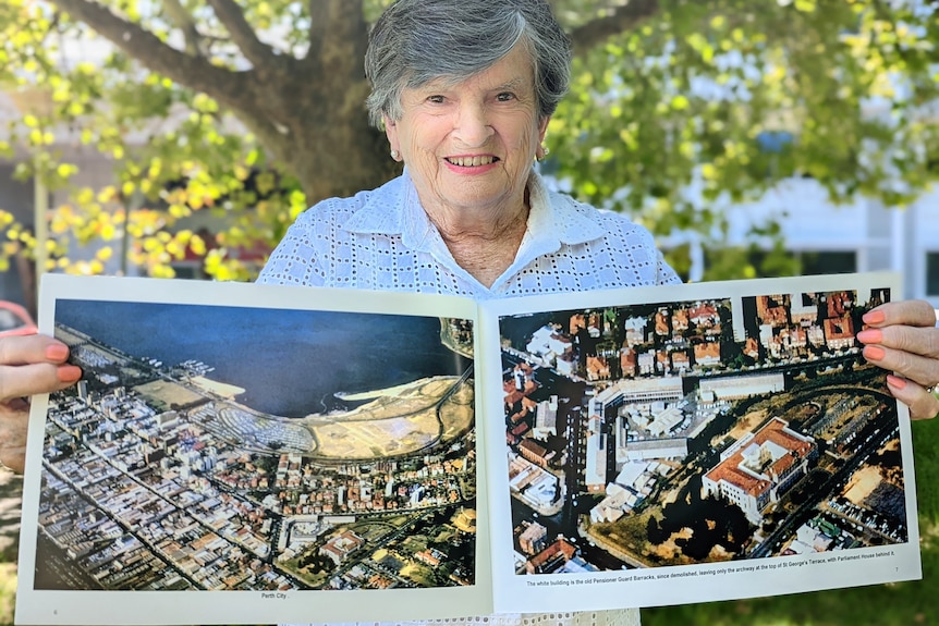 Older woman holding open a book with historic images of Perth from the air.