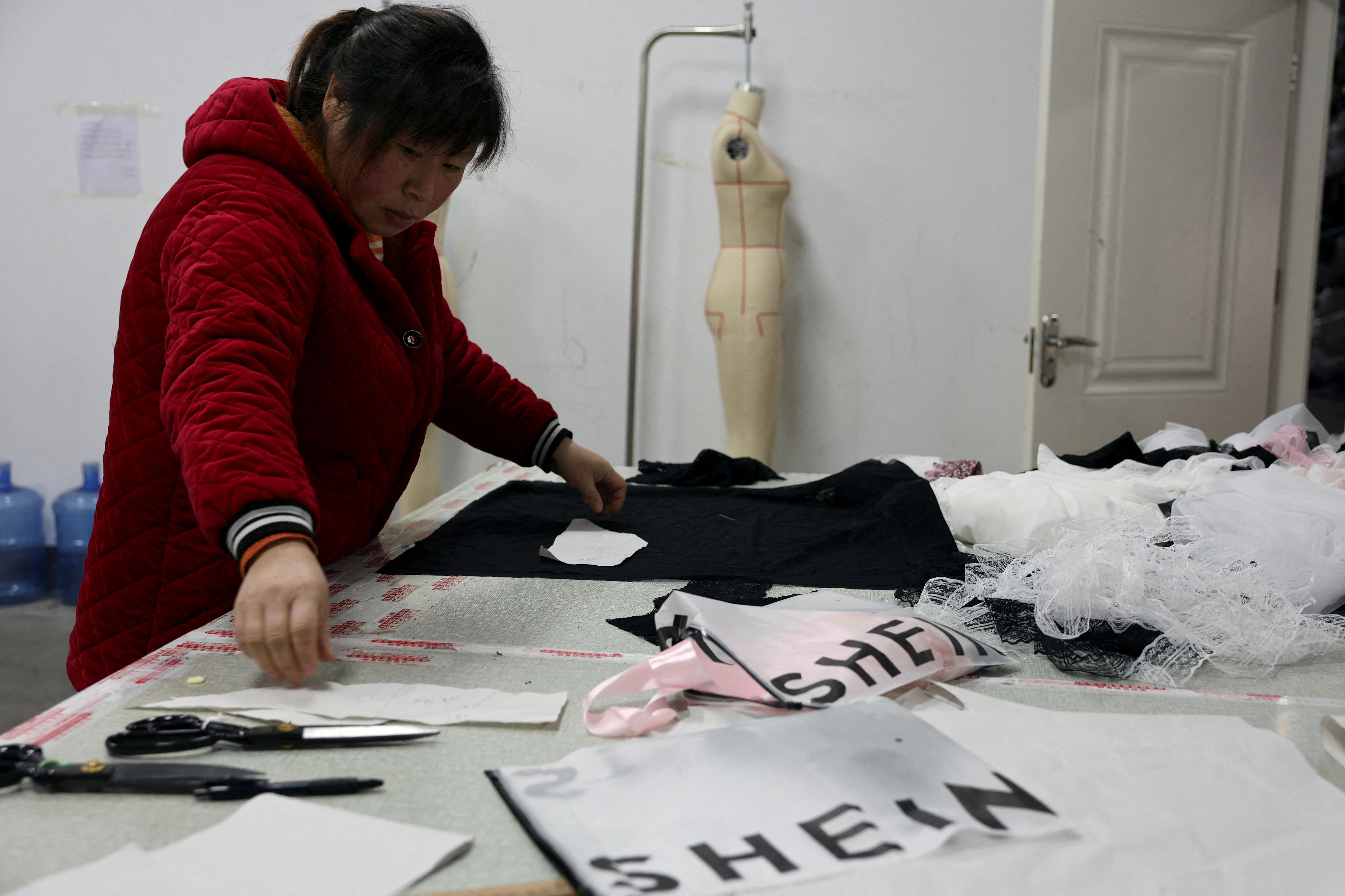 A woman lays out fabric on a table to prepare cutting it next to Shein packaging.
