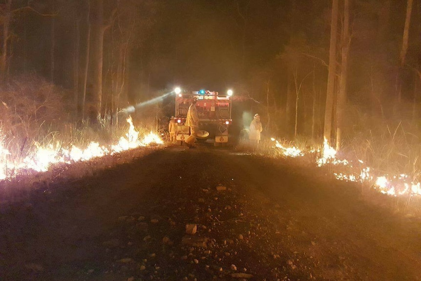 Fire fighters with a fire truck battling fire on both sides of the road.