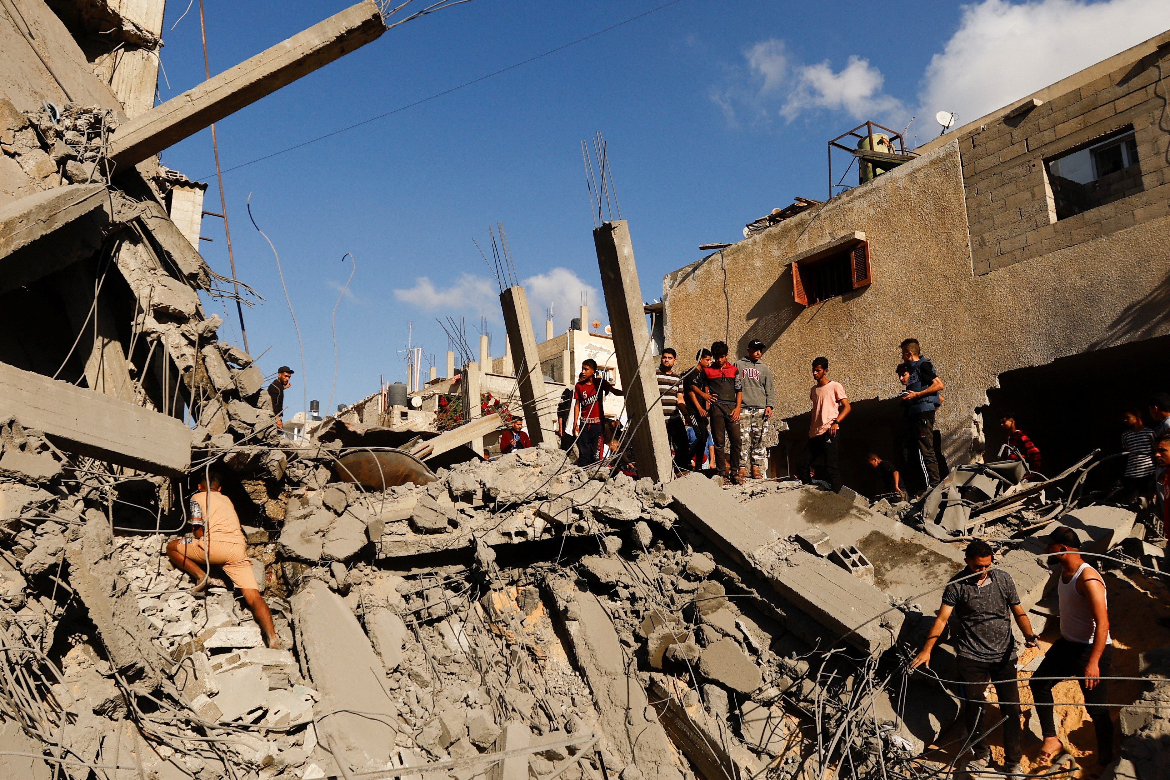 People standing on top of large piles of rubble, destroyed buildings