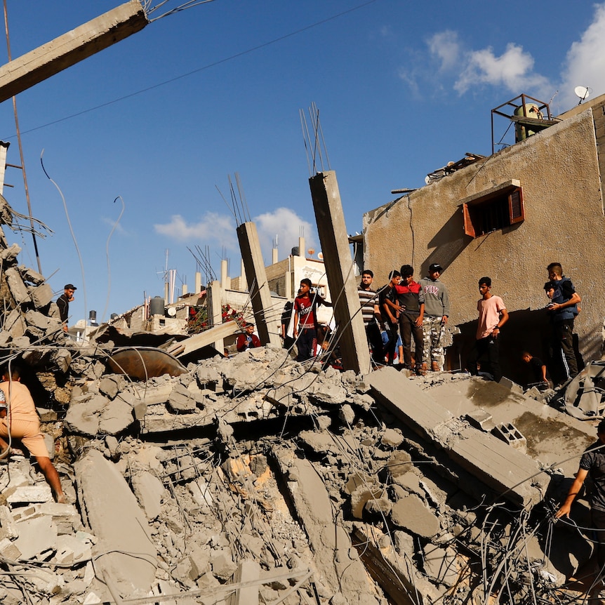 People standing on top of large piles of rubble, destroyed buildings