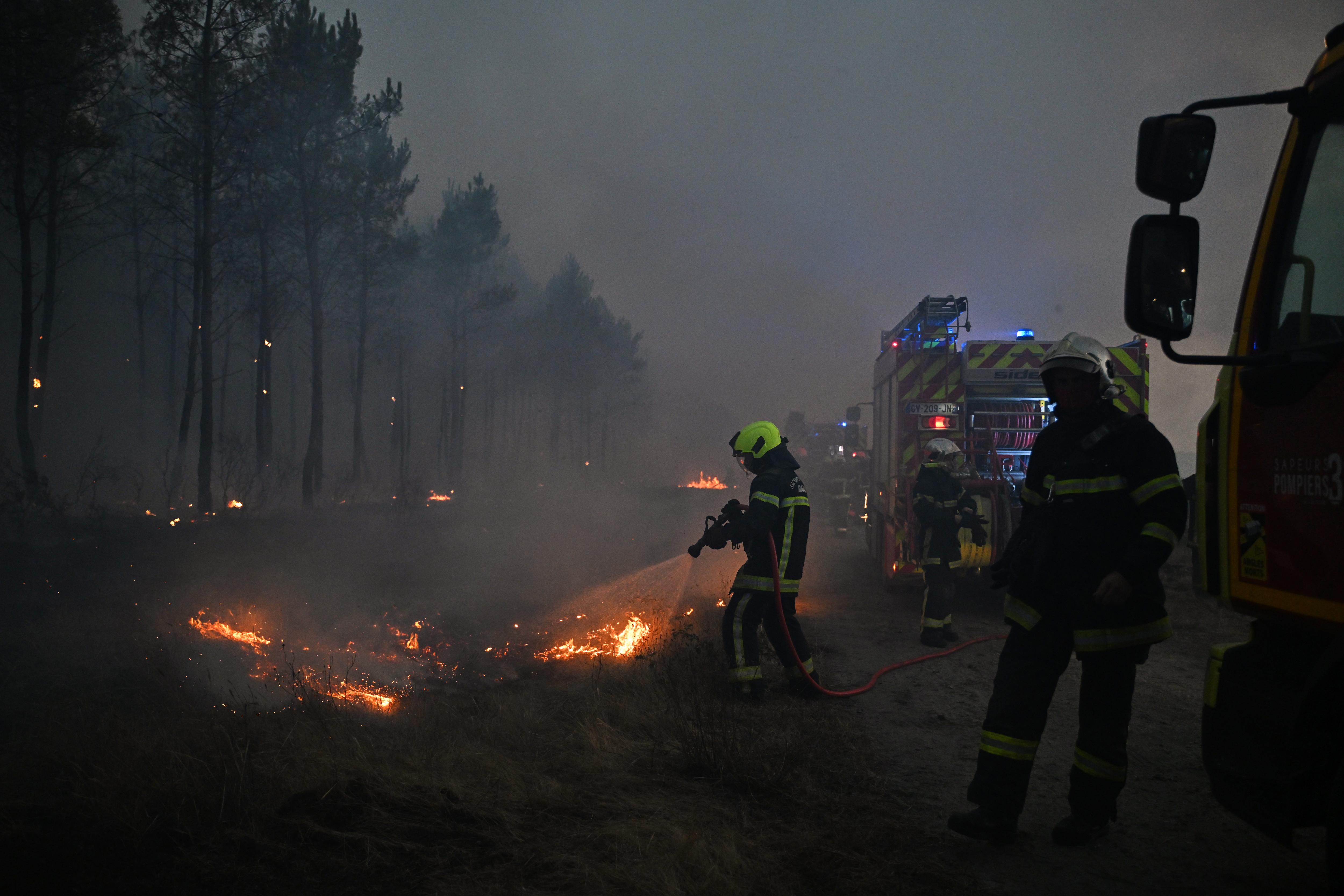 Firefighters aim a hose at flames lining the road