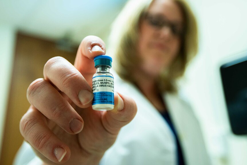 A woman holds a bottle labelled "Measles Mumps and Rubella virus"