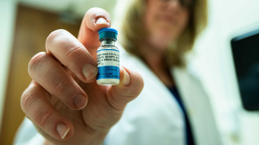 A woman holds a bottle labelled "Measles Mumps and Rubella virus"