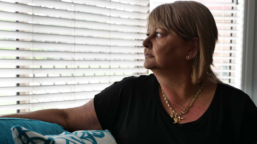 Woman sitting on the couch looks through blinds.