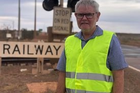 man wearing yellow fluorescent vest standing in front of lights at a railway level crossing. 