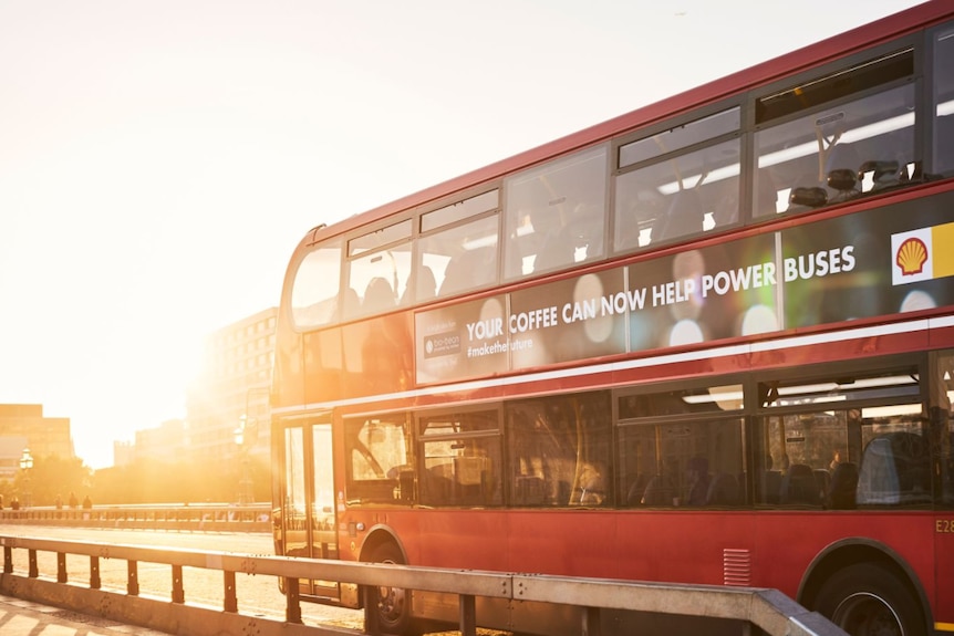 A London bus on the road with a sign saying "your coffee can now help power buses".