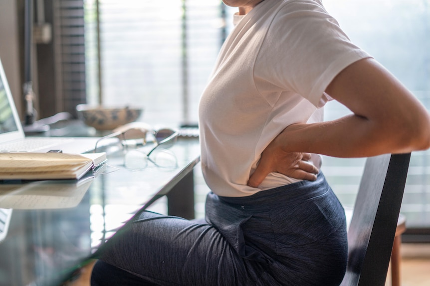 Woman holds her lower back as she sits at a desk