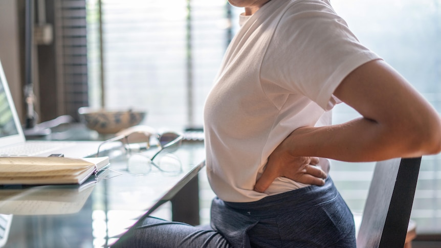 Woman holds her lower back as she sits at a desk