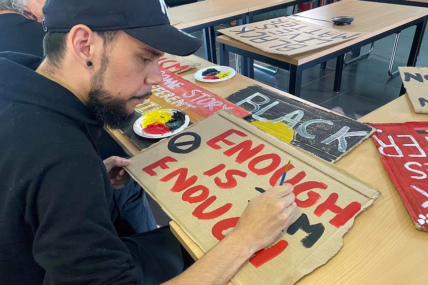 A man paints signs for a Black Lives Matter protest, with red yellow and black paint.