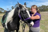 Abby Vidler, who has no forearms, standing with a black and white horse.
