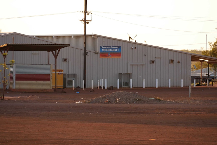 A wide shot of a supermarket in a small town, surrounded by red dirt and no trees.