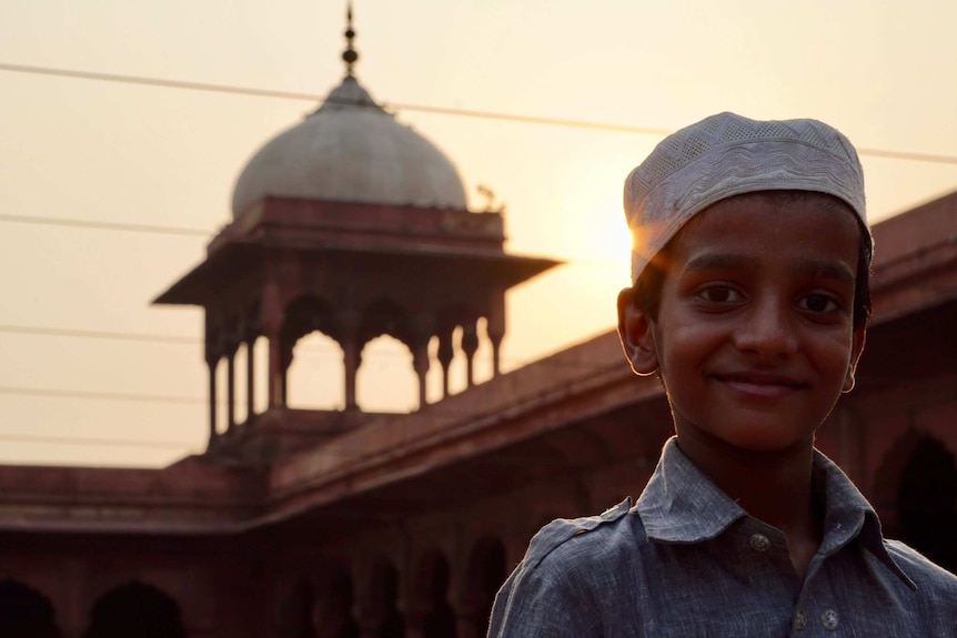 Young boy stands in front of a mosque as the sun sets.