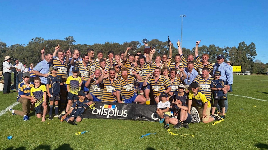 A group photo of a victorious rugby team, many with their hands raised in triumph.