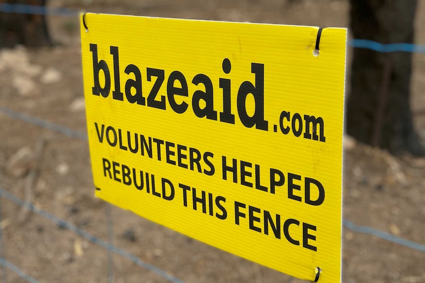 A yellow sign on a wire fence with trees behind