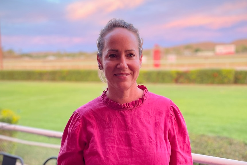 Women in pink long sleeve shirt smiles at camera whilst holding beer in hand