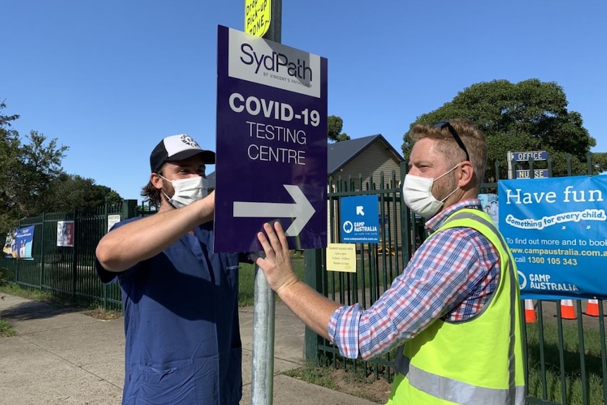 Two masked employees put a COVID-19 testing clinic sign up