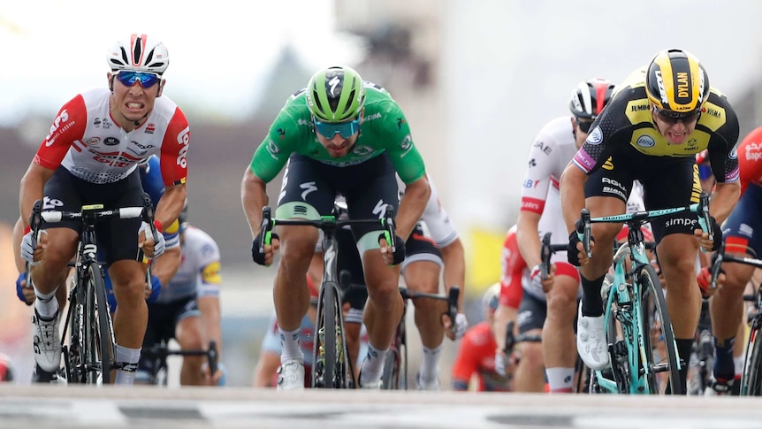 Caleb Ewan, left, grimaces as he pushes down on the pedals next to Peter Sagan in green and Dylan Groenewegen on right.